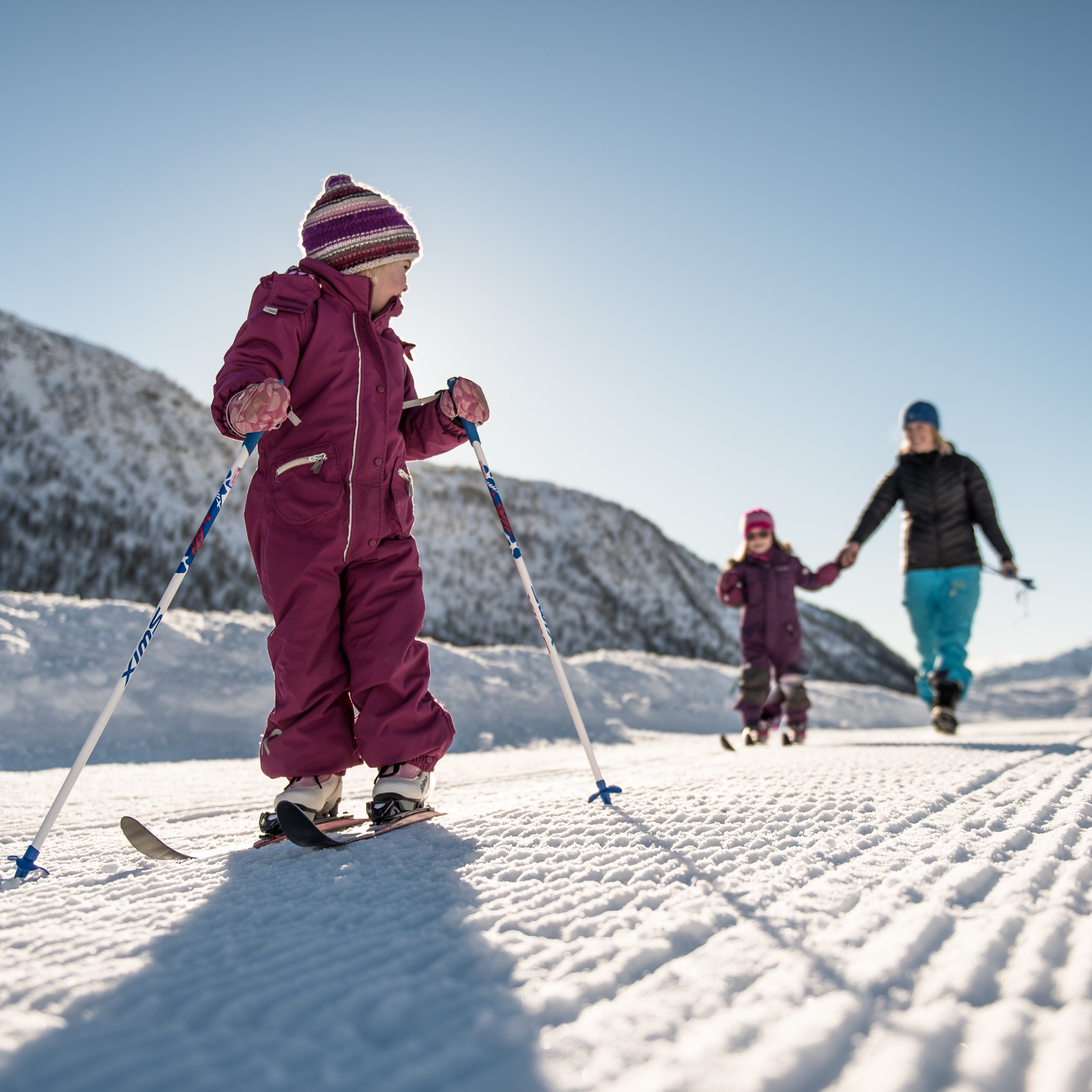 barn på langrenn i myrkdalen, i bakgrunnen går mor hånd i hånd med et annet barn