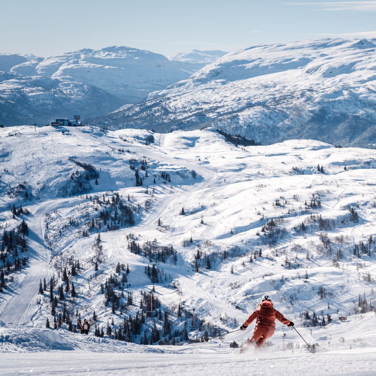 kvinne på ski i nypreppa løyper og sol, i bakgrunnen ser ein skianlegget hjå Voss Resort