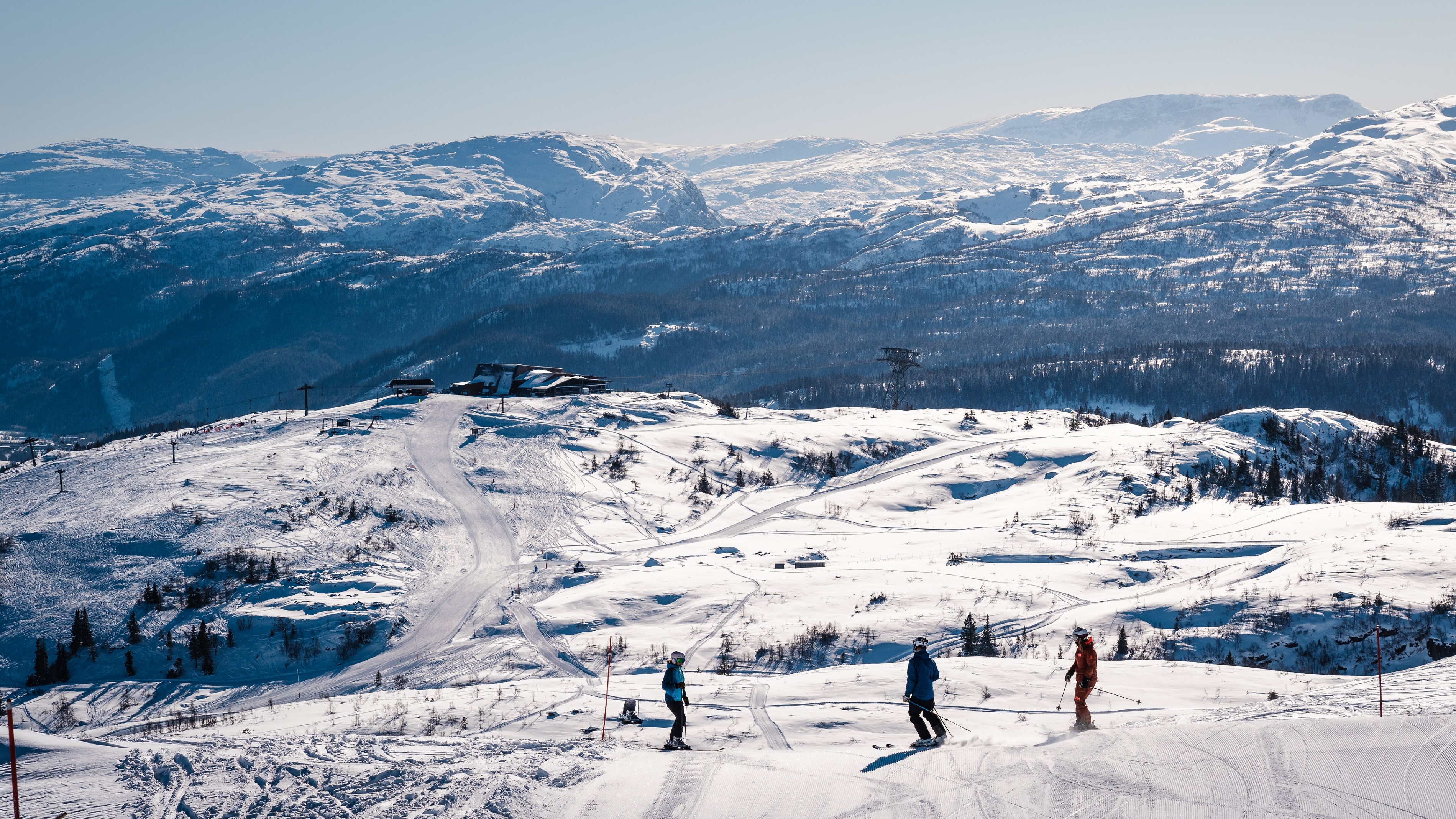 folk i bakken hos Voss resort. Solfyllte fjel og hangurstoppen i bakgrunnen 