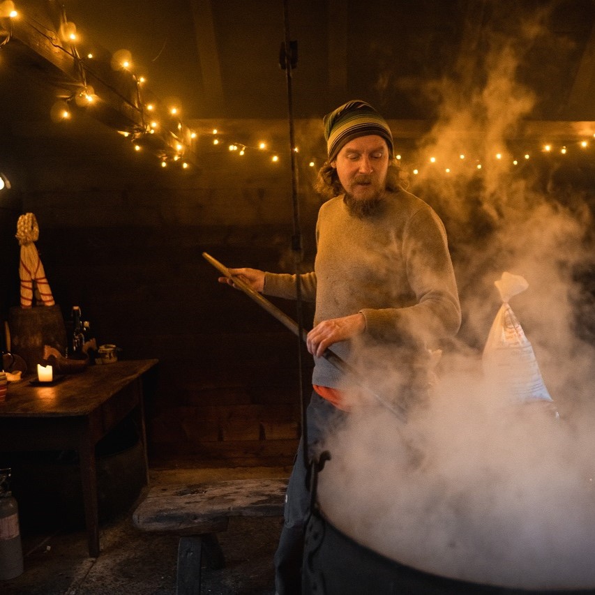 mann rører i kopperkjele, i gammalt eldhus