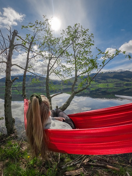 Jente som slapper av i ei hengekøye. Vangen speglar seg i vangsvatnet i bakgrunnen. 