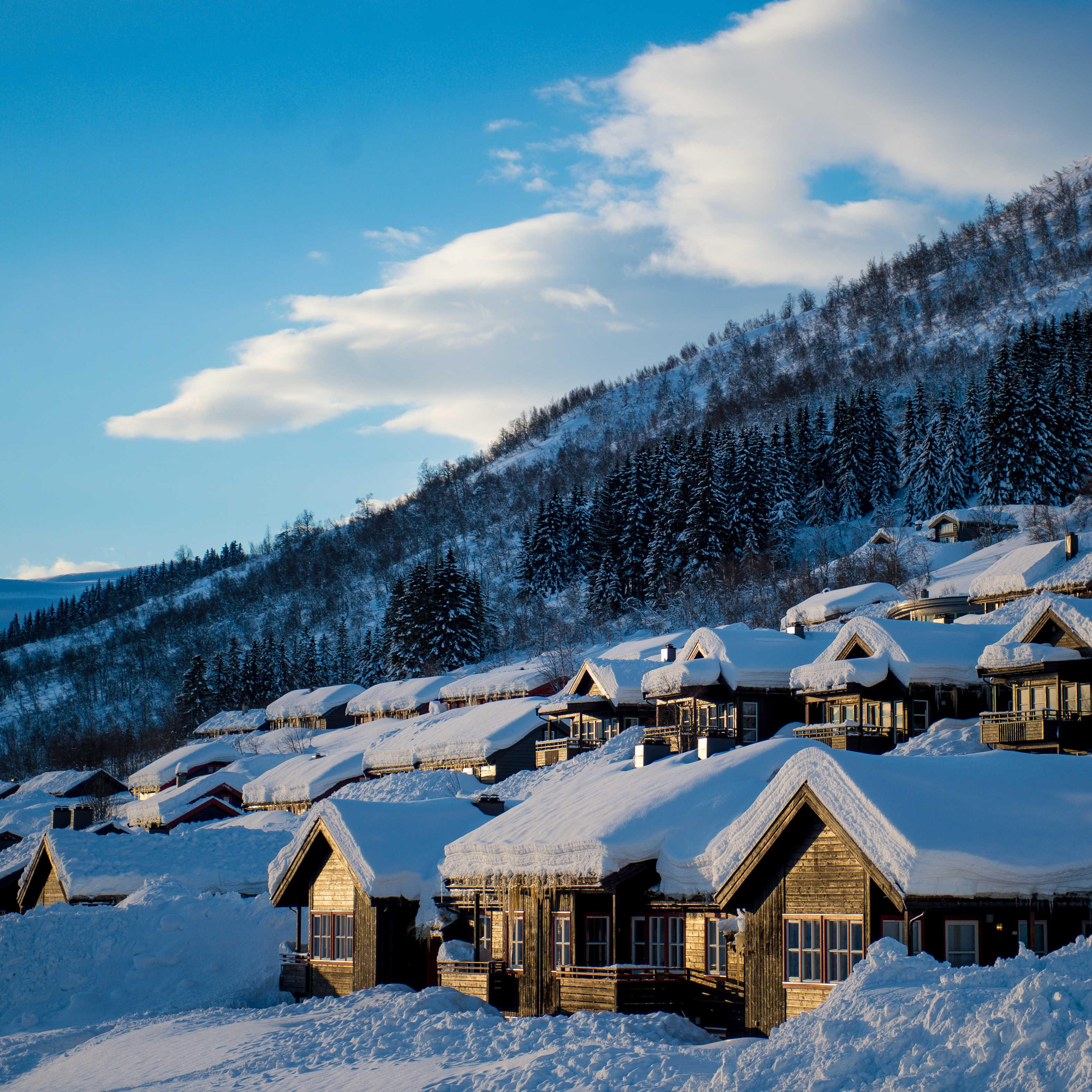 hytter i Myrkdalen med mykje snø, både på tak og og tun. I bakgrunnen ser ein fjella som tyder på at skibakken ikkje er langt unna. 