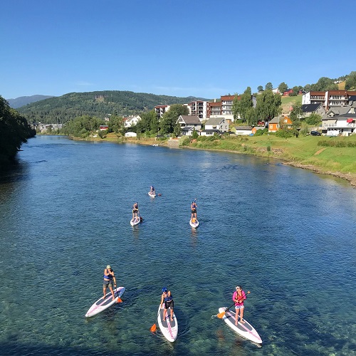 folk utforsker krystallklar, blå og grønn elv på voss med sup brett