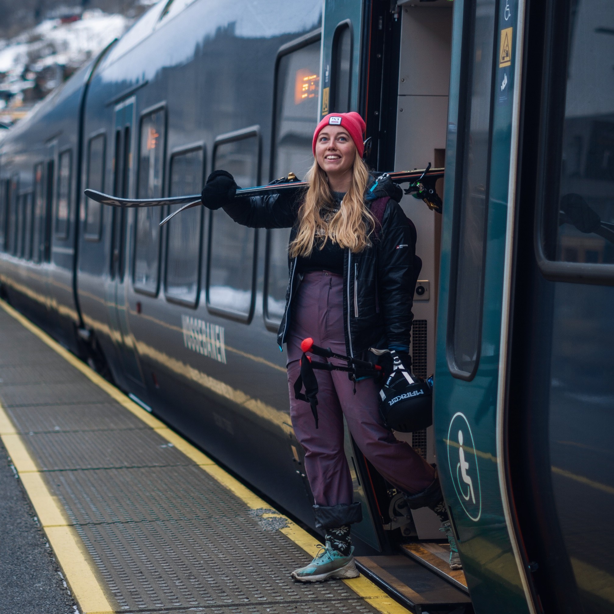 kvinne går av toget, på Voss stasjon, med skiparet over skuldrene.