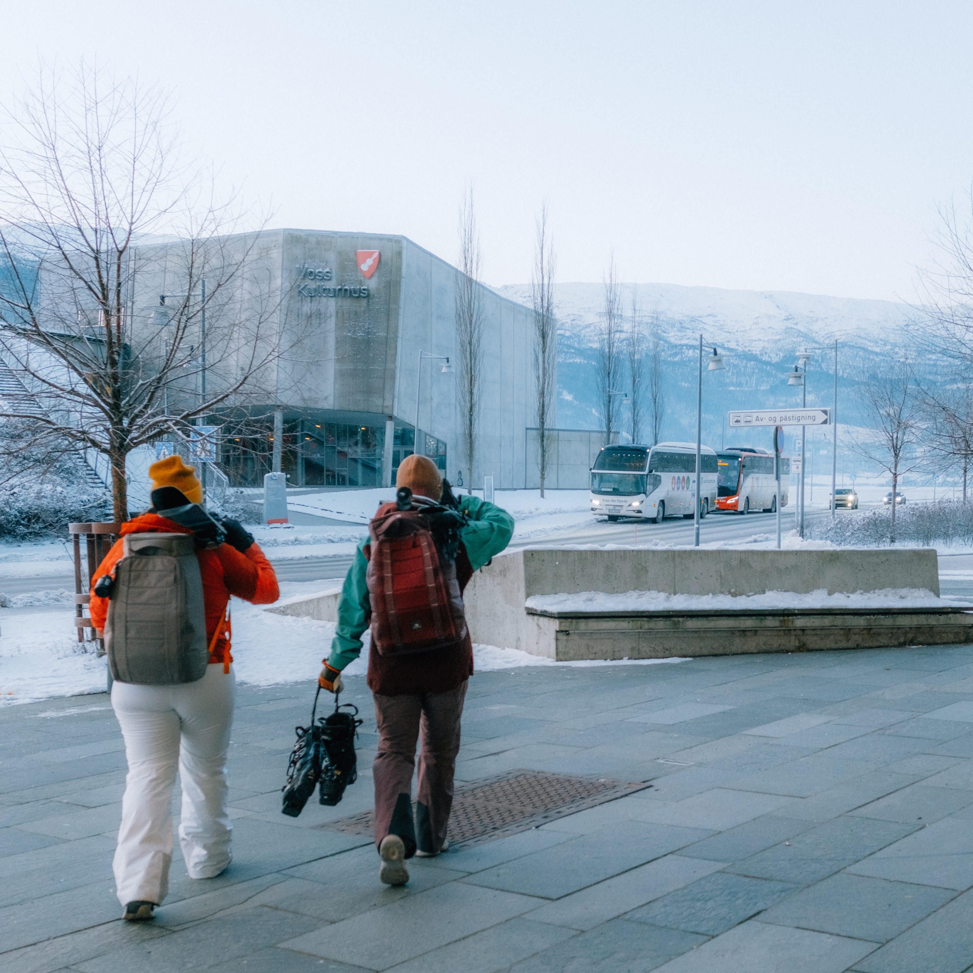 to personer med skiklær og ski, på vei til skibussen på Voss