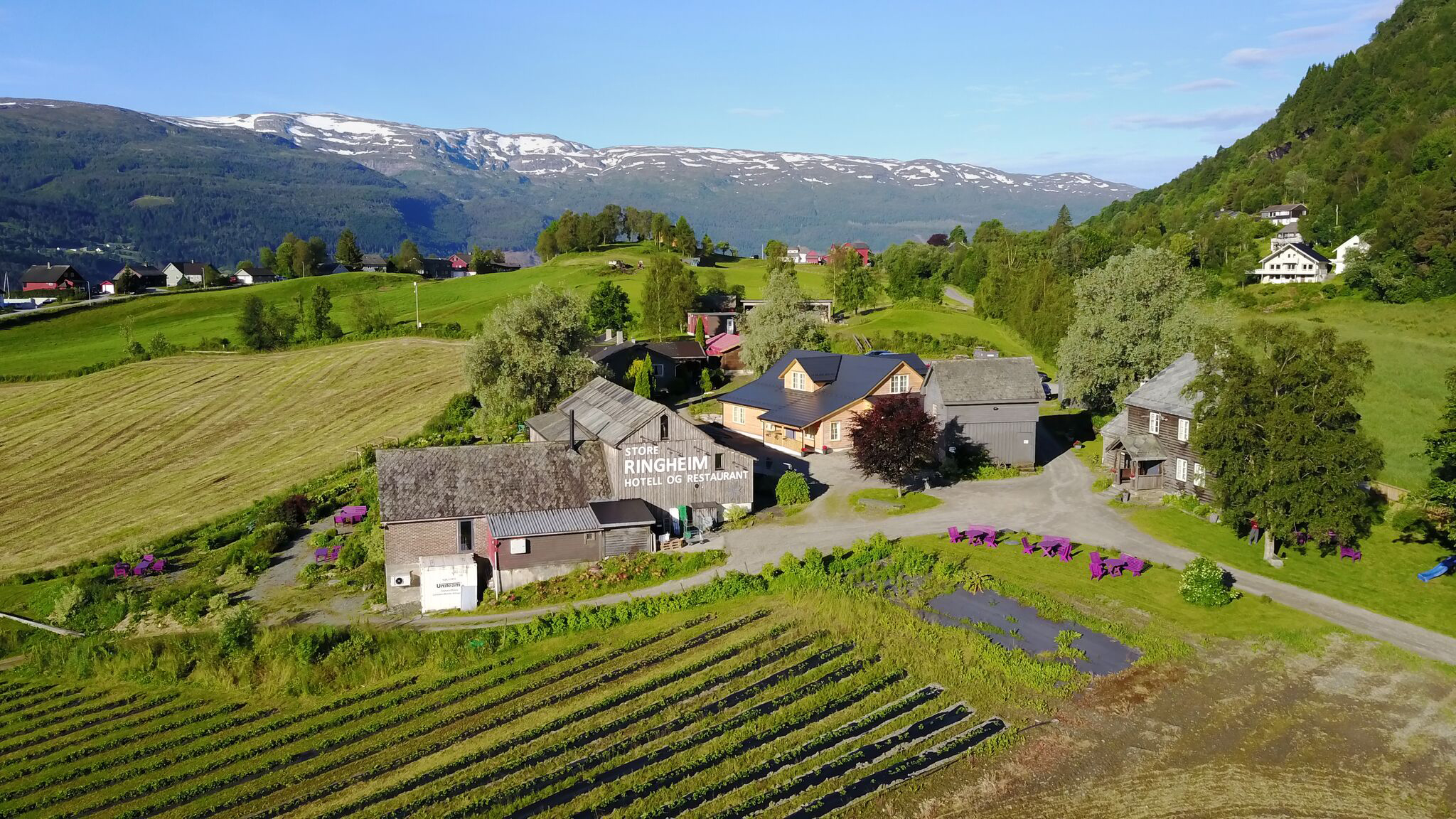 Store Ringheim hotell og restaurant omgitt av grønne bakker, sett fra drone