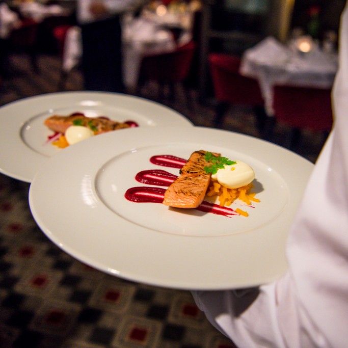 close up of two well plated meals of fish are being carried out to a restaurant, by a server. 
