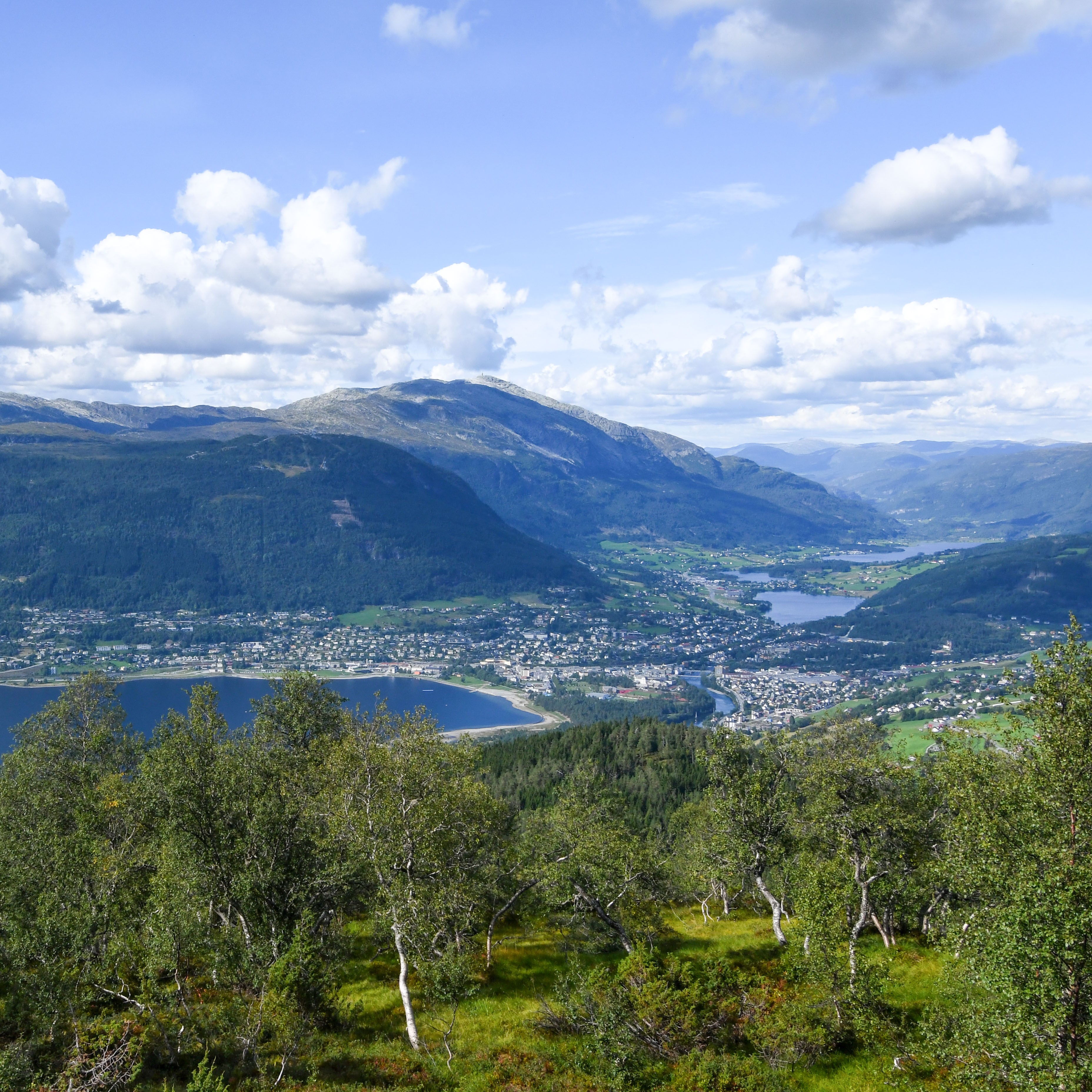 Utsikt mot Voss og Vossevangen på ein fin sommardag, med grønne landskap og sol.