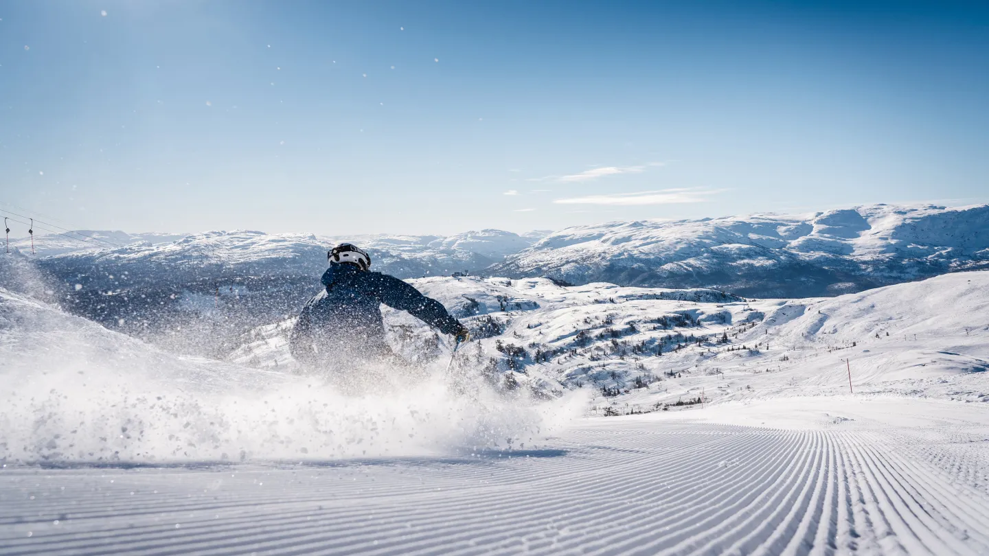 Mann på slalom i nypreppa løyper, i solskinn. 