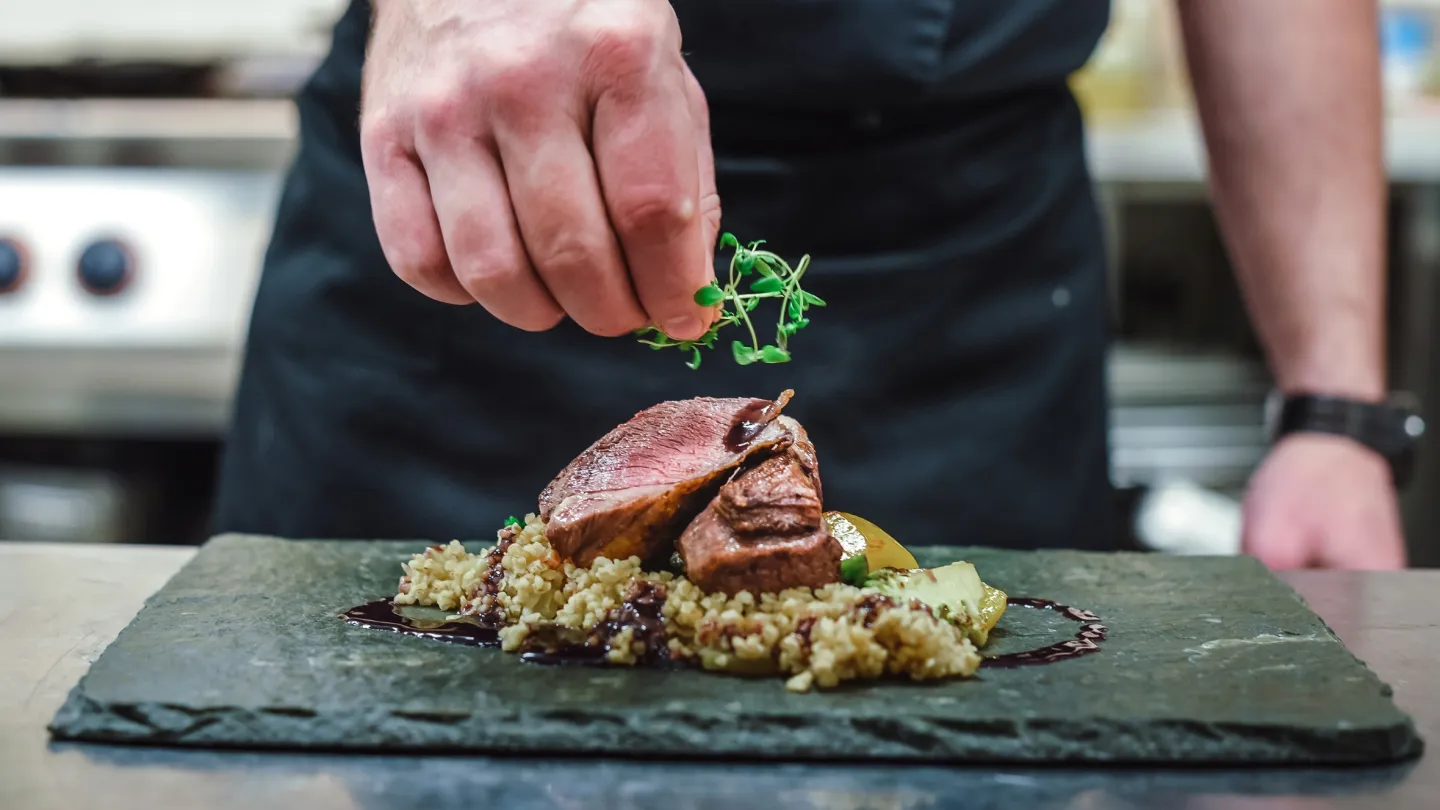 Nærbilde av hendene til en kokk som danderer en kjøttrett. 